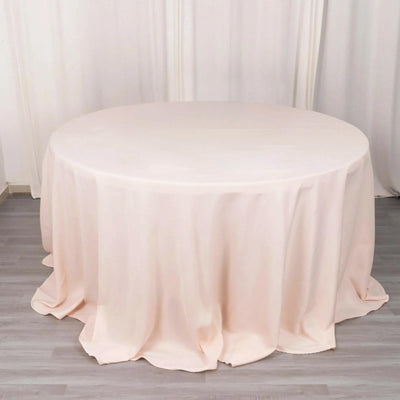 Round blush tablecloth with elegant draping on a plain backdrop.