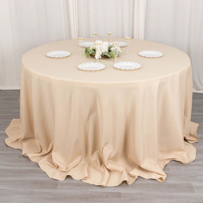 Round beige tablecloth draped elegantly over a round table with plates and candles.