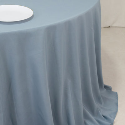 Blue tablecloth draped over a round table with a white plate on top.
