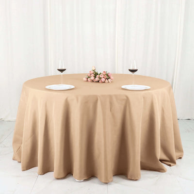 Round beige tablecloth with wine glasses and floral centerpiece.