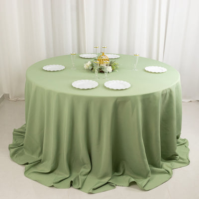 Round green tablecloth draping over a table with white plates and decorative centerpiece.