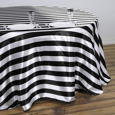 Black and white striped tablecloth draped over a round table with plates and glasses.