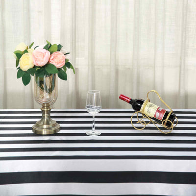 Wine bottle in a decorative holder with a glass and vase of flowers on a striped tablecloth.