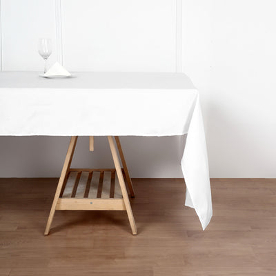 White tablecloth draped over a wooden table with a glass and napkin on top.