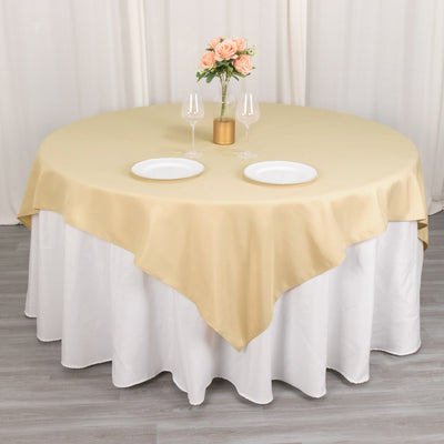 Round gold tablecloth draped over a white table with plates and flowers.