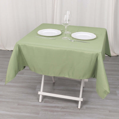 Green tablecloth draped over a table set for two with plates and cutlery.