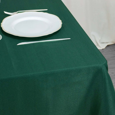 Green tablecloth with a white plate and cutlery arranged on a dining table.
