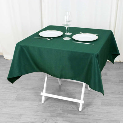Green tablecloth on a dining table with plates and a glass.