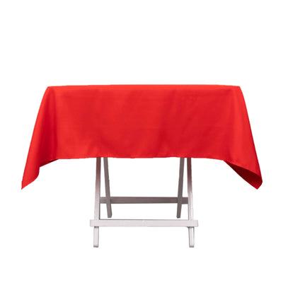 Red tablecloth draped over a folding table on a plain backdrop.