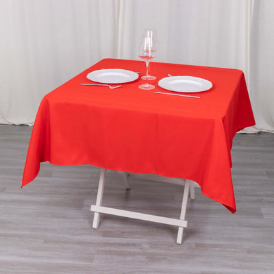 Red tablecloth draped over a folding table with plates and a wine glass.