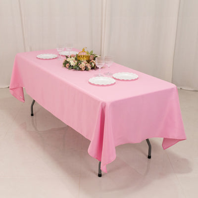 Pink tablecloth draped over a folding table set for a gathering with plates and flowers.