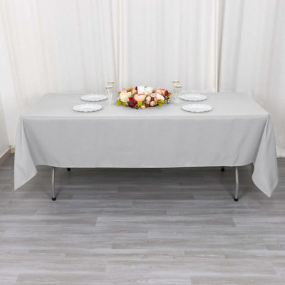 Gray tablecloth draped over a table set for a gathering with flowers and plates.