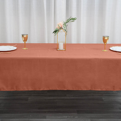 Elegant rust-colored tablecloth with gold accents and floral centerpiece on a dining table.