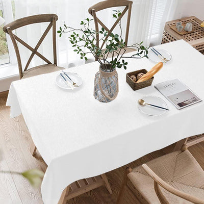 White tablecloth on a dining table set with plates and a vase of greenery.