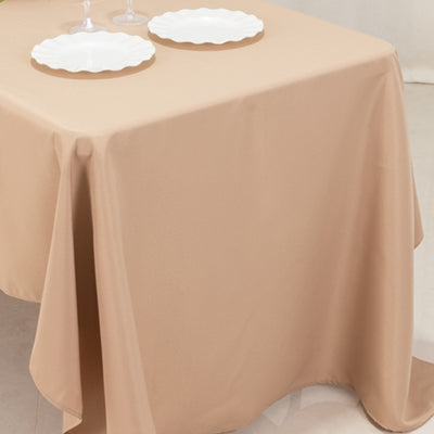 Beige tablecloth draped over a table with two white plates on top.