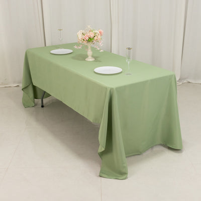 Green tablecloth draped over a table set for two with plates and glasses.