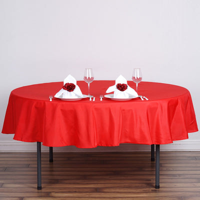 Round red tablecloth set for dining with elegant napkins and glassware.