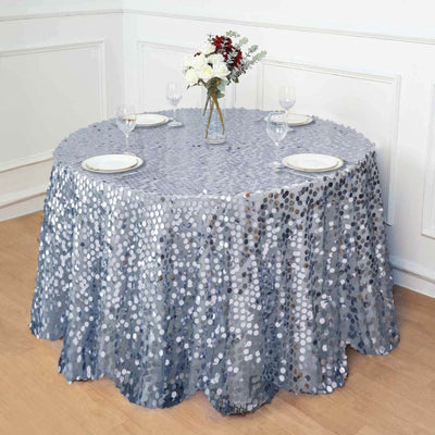 Round silver sequin tablecloth draped over a dining table with plates and flowers.