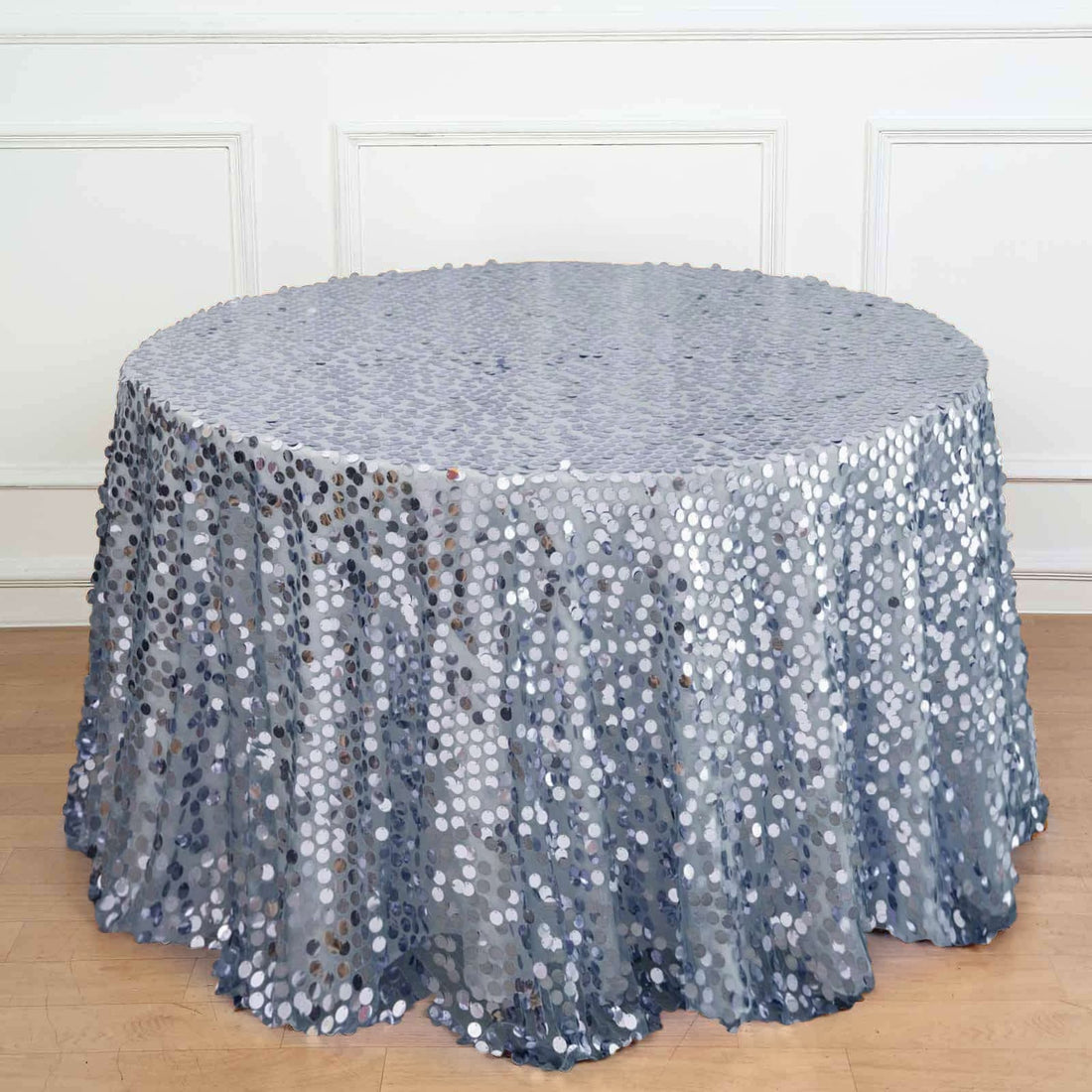 Round silver sequin tablecloth on a wooden surface.