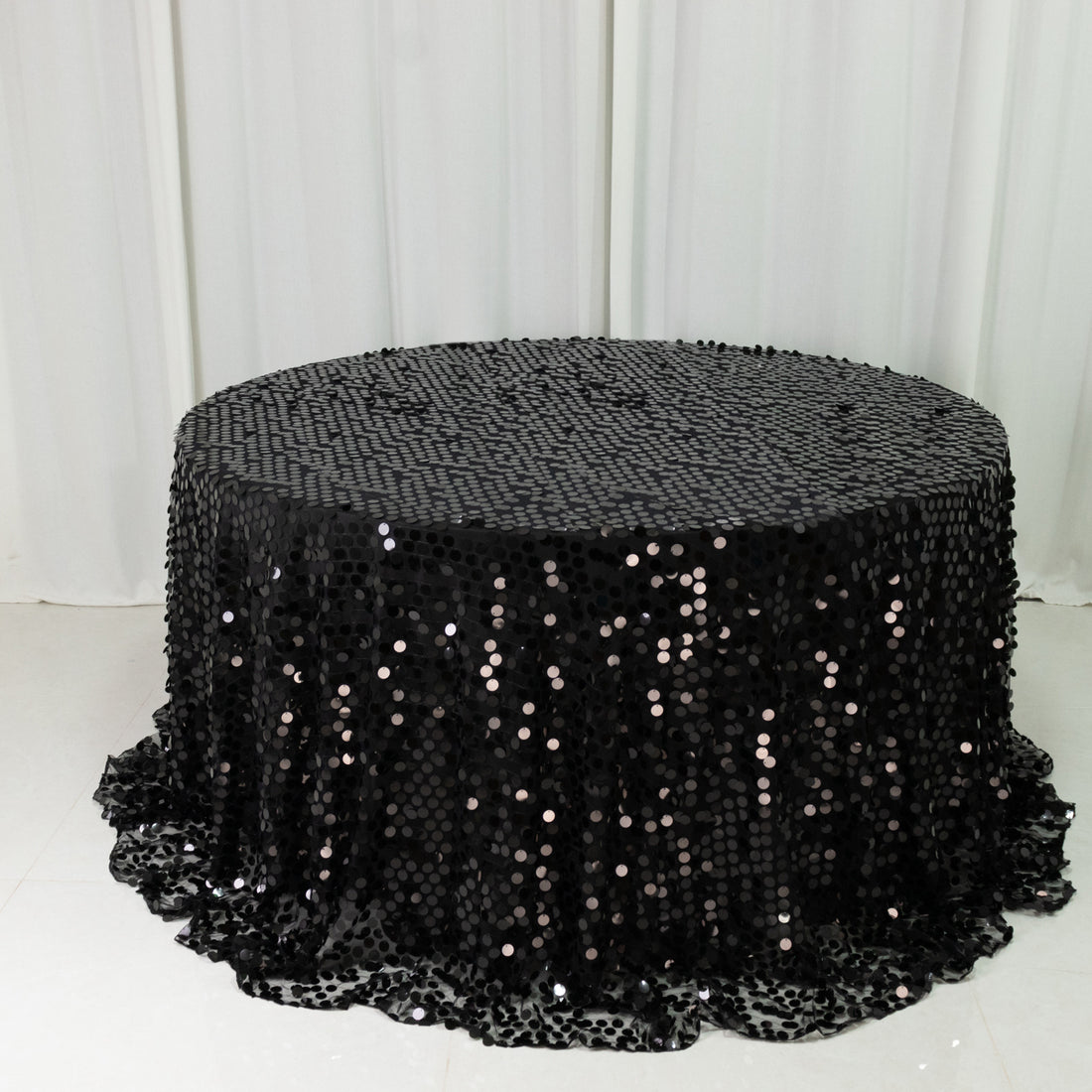 Black sequin tablecloth draped over a round table in a studio setting.