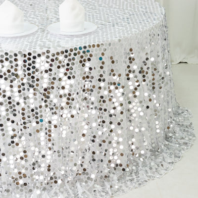 Silver sequin tablecloth on a round table with white plates.