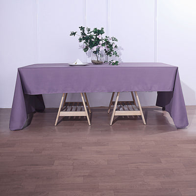 Purple tablecloth draped over a wooden table with flowers in a vase.