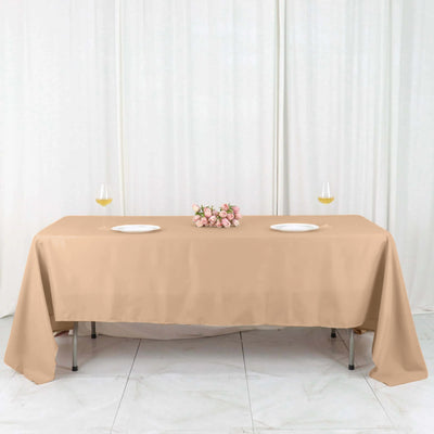 Beige tablecloth draped over a table with plates and flowers.