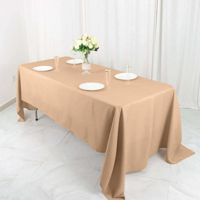 Beige tablecloth draped over a table set with plates and floral centerpiece.
