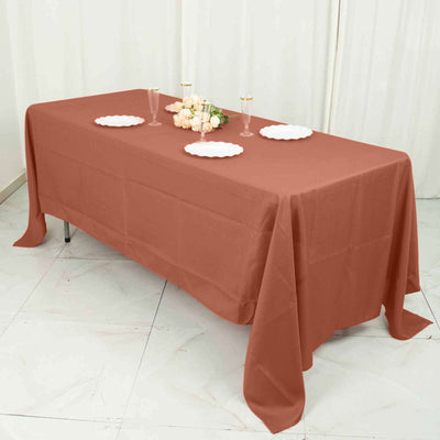 Rust-colored tablecloth draped over a table set with plates and floral arrangement.