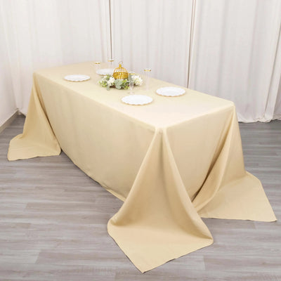 Beige tablecloth draped over a dining table with decorative plates and floral arrangement.