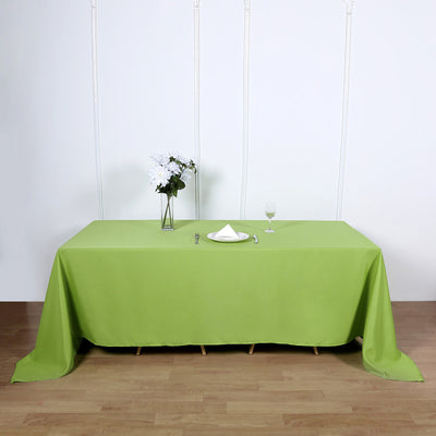 Green tablecloth on a wooden table with a vase and glass.