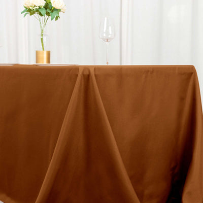 Brown tablecloth draped over a table with a glass and vase of flowers.
