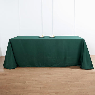Green tablecloth draped over a table with candle holders on a plain backdrop.