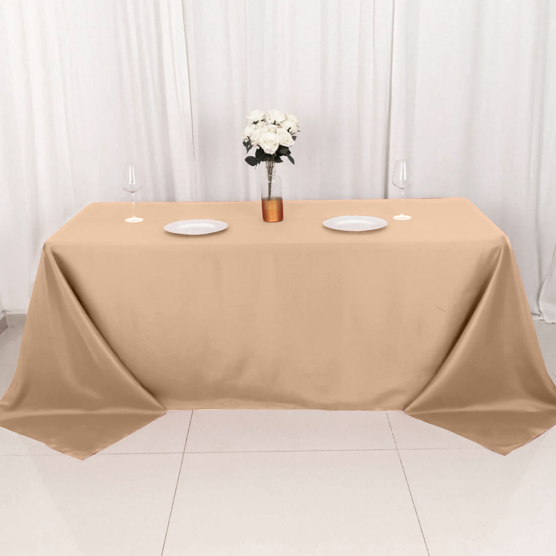 Beige tablecloth draped over a table with plates and a vase of flowers.