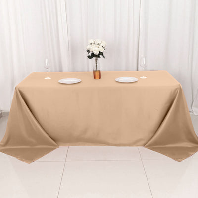 Beige tablecloth draped over a table with plates and a vase of flowers.