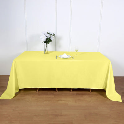 Yellow tablecloth on a wooden table with a vase and glass.