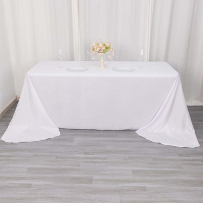 White tablecloth draped over a table with floral centerpiece and plates.