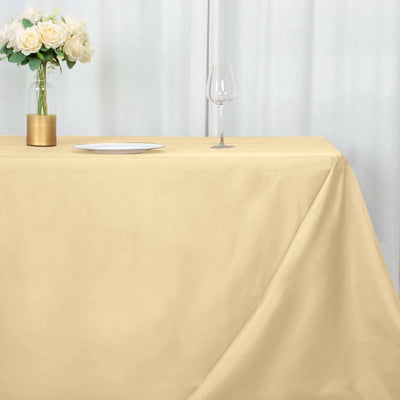 Beige tablecloth draped over a table with a vase and wine glass on a neutral background.