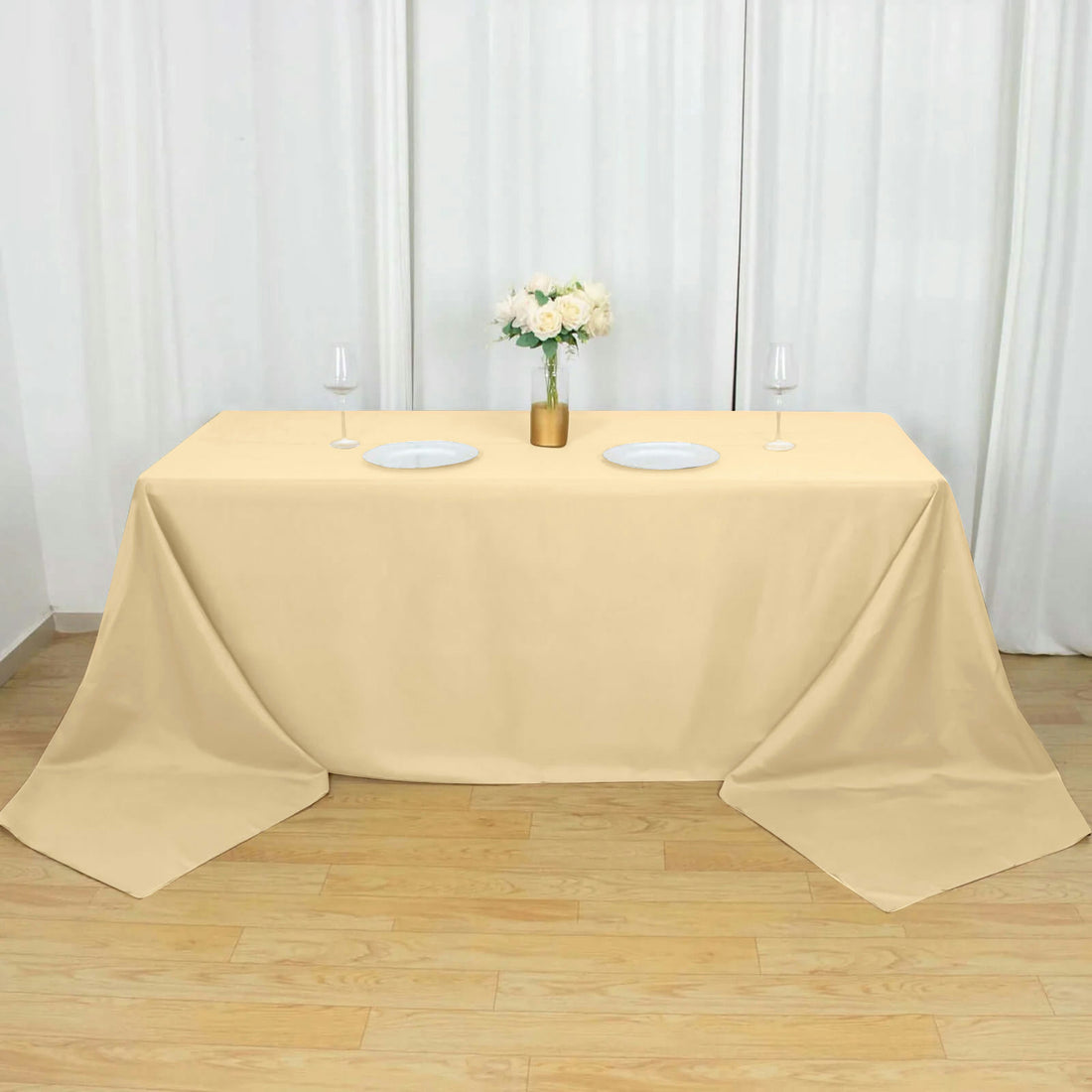 Beige tablecloth draped over a table with plates and a floral centerpiece.