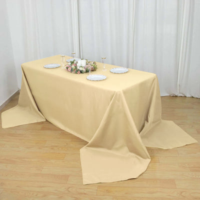 Beige tablecloth draping over a table set with plates and floral centerpiece.