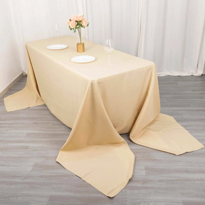 Elegant beige tablecloth draped on a table with plates and floral centerpiece.