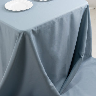 Blue tablecloth draped over a table with white plates on a light backdrop.