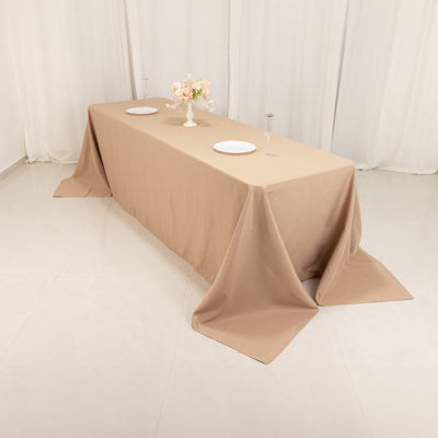 Beige tablecloth draped over a long table with plates and a flower vase.