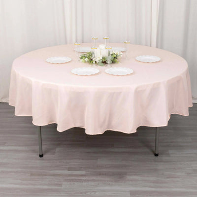 Round pink tablecloth draped over a table with decorative plates and candles.
