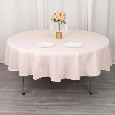 Round blush tablecloth draped elegantly over a table with plates and flowers.
