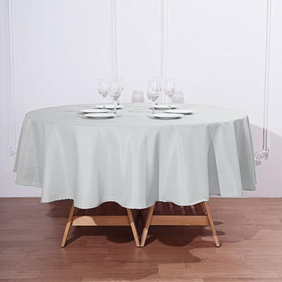 Round gray tablecloth draped over a wooden table with plates and glasses.