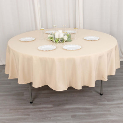 Round beige tablecloth draped over a circular table with decorative plates and candles.