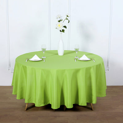 Round green tablecloth on a dining table with glasses and napkins.