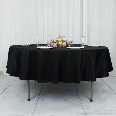 Black tablecloth draped over a round table set with elegant tableware and floral decor.
