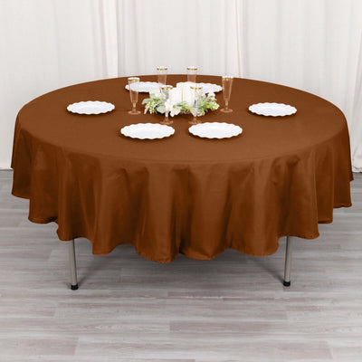 Brown round tablecloth on a dining table with plates and glasses.